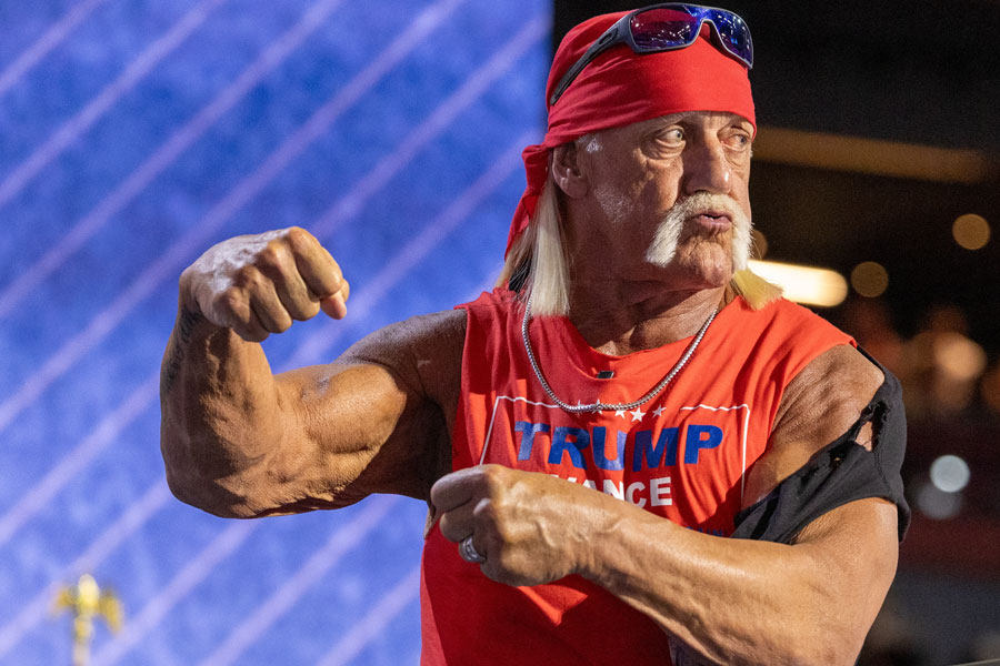 Wrestling icon Hulk Hogan, wearing a red bandana, sunglasses, and a sleeveless "Trump Pence" shirt, flexes his muscles during a public appearance at the 2024 RNC in Milwaukee. The image captures Hogan’s trademark charisma and larger-than-life persona in one of his final major public moments.