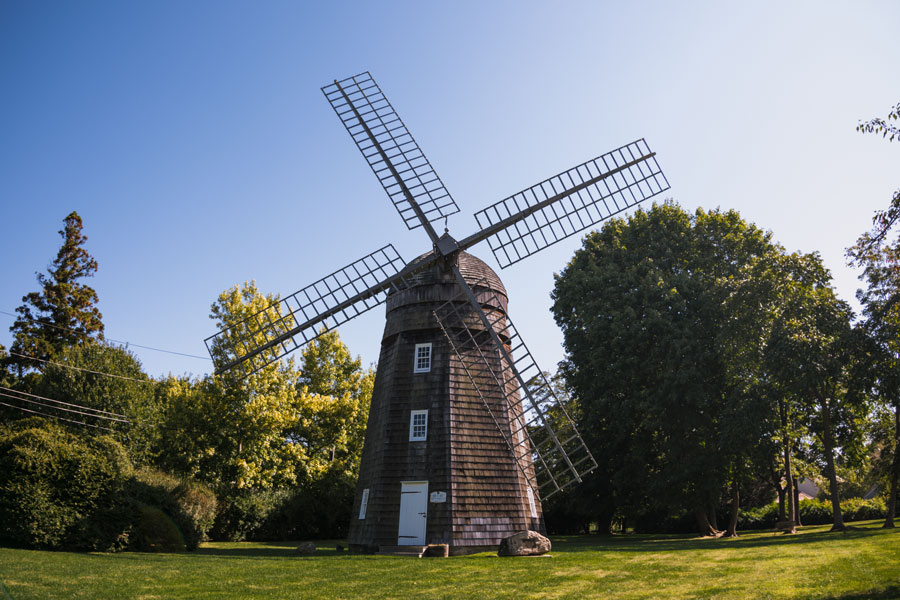 Historic Beebe Windmill set against lush summer greenery and a vibrant blue sky in Bridgehampton, New York.