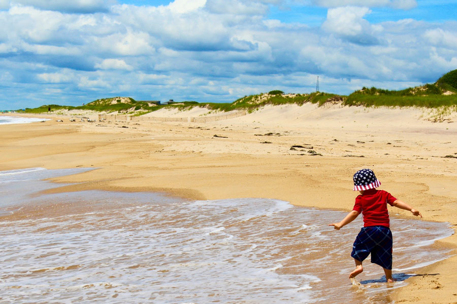 The wide-open shoreline and natural dunes highlight the unspoiled beauty of Hither Hills, known for its family-friendly beaches, scenic landscapes, and peaceful atmosphere. The image evokes a sense of carefree fun and the timeless joy of a day at the beach. 