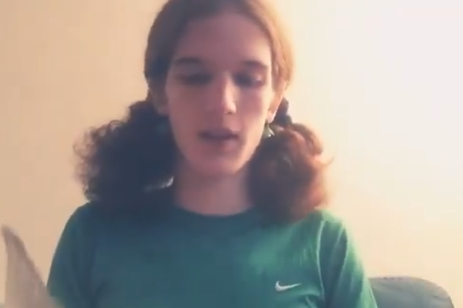 An image circulating online shows 23-year-old Robin Westman, dressed in a green Nike t-shirt with hair tied in pigtails, appearing on camera while reading from a document. Authorities have confirmed Westman as the individual responsible for the deadly shooting at Annunciation Catholic Church and School in Minneapolis.