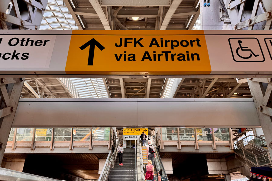 Sign for “JFK Airport via AirTrain” at Jamaica Station, one of the busiest transit hubs in Queens, New York City. Jamaica Station connects the Long Island Rail Road (LIRR), numerous subway lines, and city buses, making it the primary transfer point for travelers heading to John F. Kennedy International Airport. The AirTrain JFK is a dedicated people mover that links the station directly to all airport terminals, providing convenient rail access for local commuters and international travelers. 