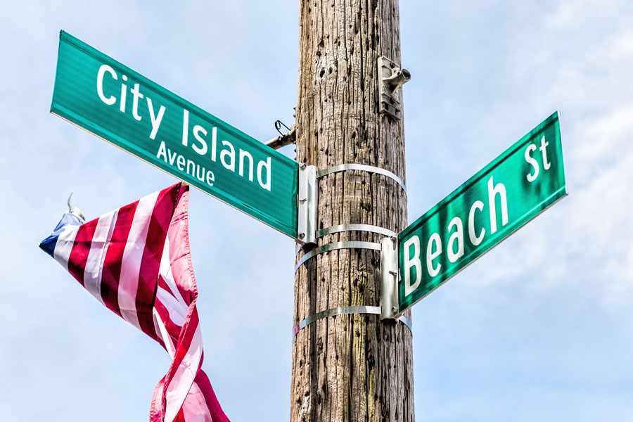 City Island Avenue and Beach street signs at intersection in Bronx, New York City, NYC with american flag
