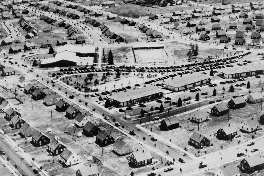 This is an aerial photograph of Levittown, New York from around 1953, showcasing the early days of this iconic planned suburban community on Long Island, named after its builder William Levitt. The community was built between 1947 and 1951 to accommodate returning veterans and their families, featuring uniformly designed houses and a distinct curvilinear street layout, as seen in the image. 