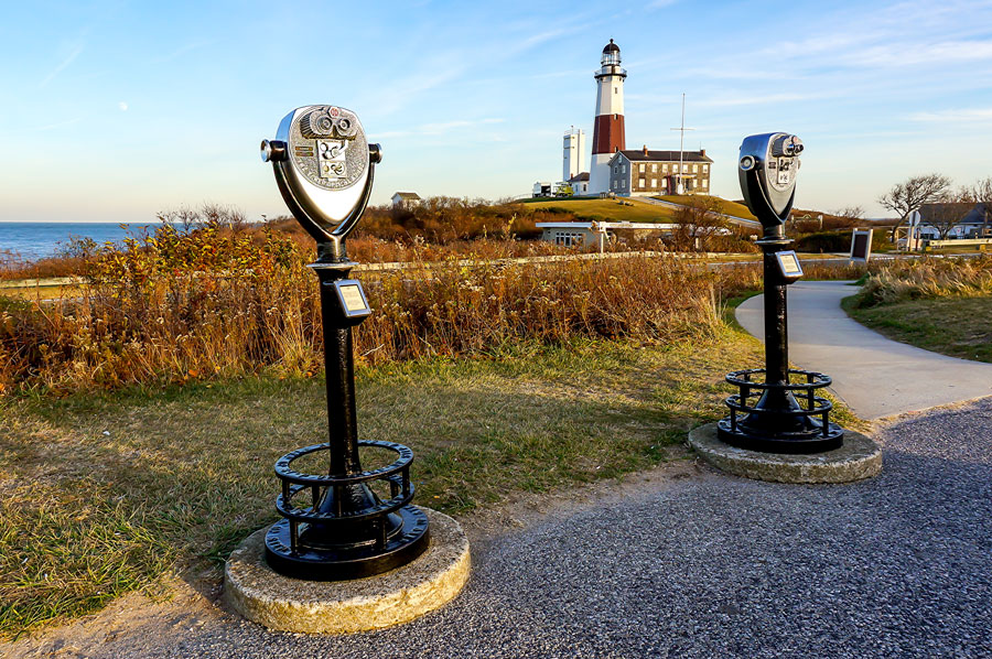 Two classic coin-operated binocular viewers invite visitors to take in sweeping panoramic views of the Atlantic Ocean and rugged coastline. The gently curving path and vibrant natural landscape highlight Montauk’s enduring appeal as a scenic, historic landmark and a favorite destination in the Hamptons, especially during the crisp, golden days of autumn.