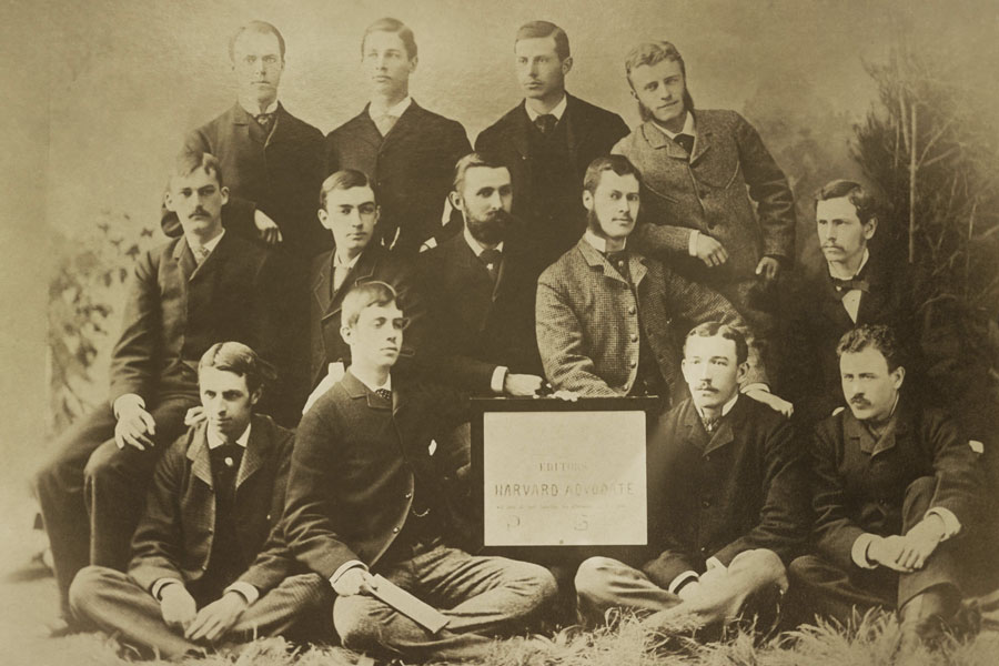 Theodore Roosevelt standing at right, smiling, and leaning in. He posed with his fellow editors of the Harvard Advocate Editorial Board in 1880. Seated in center is historian, Albert Bushnell Hart