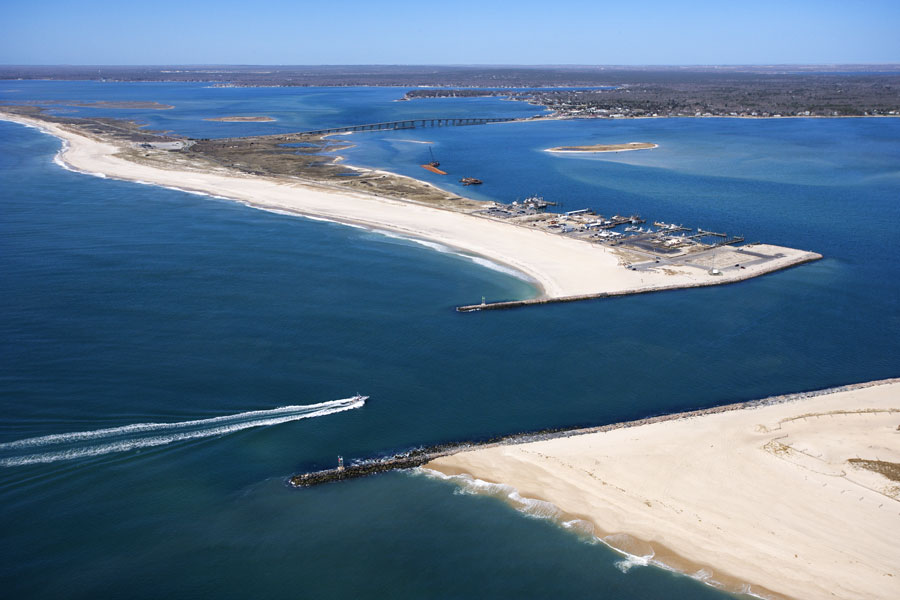 A stunning aerial view of Shinnecock Bay on Long Island’s East End, showcasing its sweeping sandy shores, crystal blue waters, and the inlet connecting the bay to the Atlantic Ocean. The bay is a haven for boaters, fishermen, and water sports enthusiasts, and is surrounded by scenic barrier beaches, wildlife habitats, and vibrant local communities. Shinnecock Bay is a central feature of the area’s natural beauty and a gateway to both Southampton and the broader Hamptons region.
