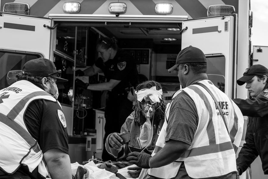 Emergency personnel from the Wyandanch-Wheatley Heights Ambulance Corps rush a gunshot victim to an ambulance. The black and white image captures paramedics and first responders working quickly at the scene, highlighting the urgency and bravery involved in life-saving efforts. File photo: Joseph Cassano, licensed.