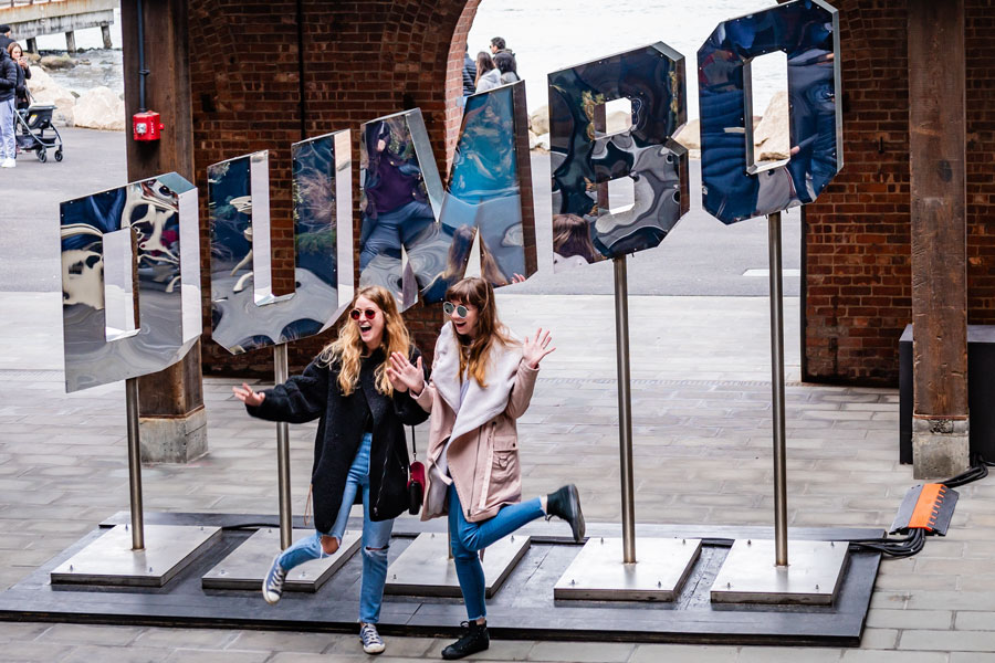 Visitors pose in front of the mirrored DUMBO sign in Brooklyn, New York. The neighborhood, whose name stands for ‘Down Under the Manhattan Bridge Overpass,’ has become a popular destination for photos, waterfront views, and artsy, industrial-chic vibes.