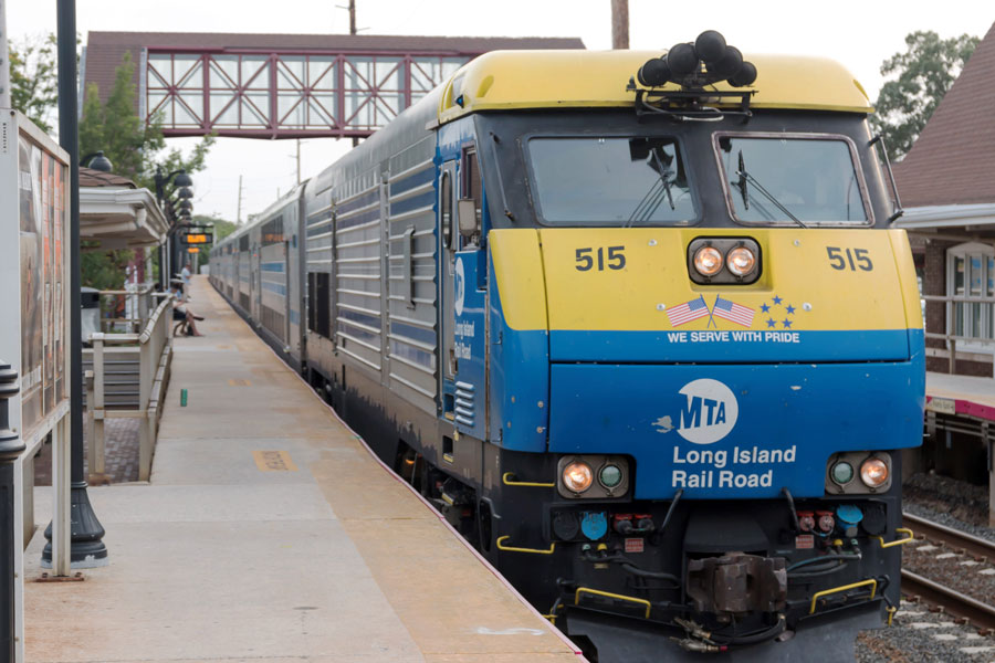 A Long Island Rail Road (LIRR) train prominently displays the blue and yellow MTA LIRR branding, along with the number 515. Above the logo is a banner reading "We Serve With Pride" and decorated with American flags and stars. The train in this image looks different from many other Long Island Rail Road trains because the LIRR operates several types of trainsets, including both electric and diesel-powered fleets, each with distinct appearances and uses. 