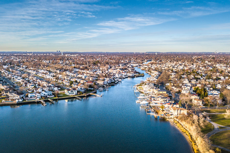 Aerial drone view of Long Island’s South Shore at sunset, showcasing canal-front homes and winding waterways that open into the Great South Bay. The image highlights the region’s coastal lifestyle, where boating, fishing, and waterfront living are central to community life.