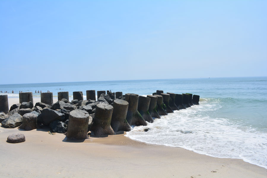 Remnants of an old fishing dock made of concrete and rocks along the beach at Ocean Beach, Fire Island, New York, with calm Atlantic Ocean waves under a clear blue sky.