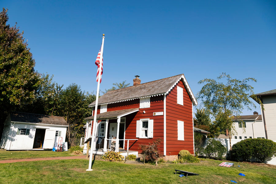 Historic red farmhouse with white trim and an American flag on the lawn in North Massapequa, Long Island, New York, under a bright blue sky.