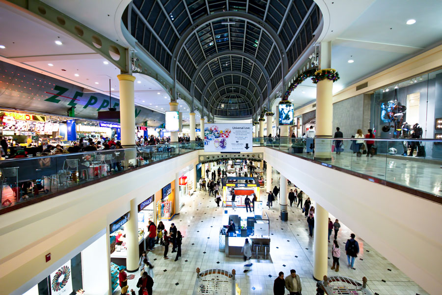 Wide interior view of Roosevelt Field Mall in Garden City, New York, showing shoppers walking through the main concourse under a tall glass-domed ceiling with two levels of stores and restaurants.