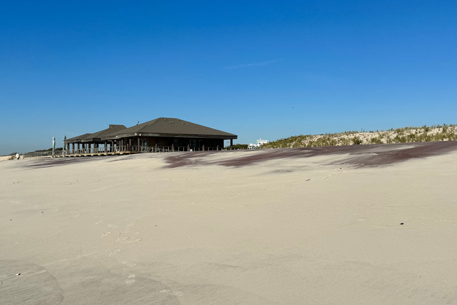 Wide sandy beach with the Tobay Beach pavilion and boardwalk in the background under a clear blue sky on Long Island’s South Shore in the Town of Oyster Bay, New York.