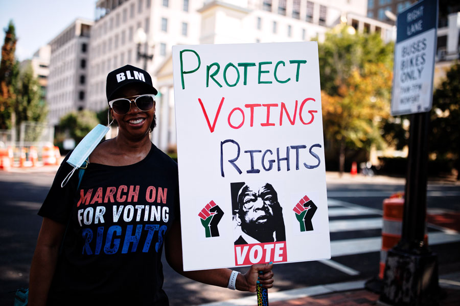 Person wearing a March On for Voting Rights shirt and BLM cap holds a sign reading Protect Voting Rights during a street protest advocating for voting rights protections in Washington, D.C.