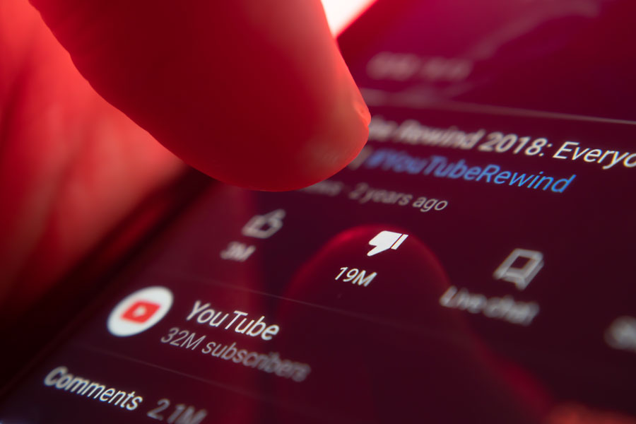Close-up of a finger pressing the dislike icon on a smartphone screen showing a YouTube video with millions of dislikes.