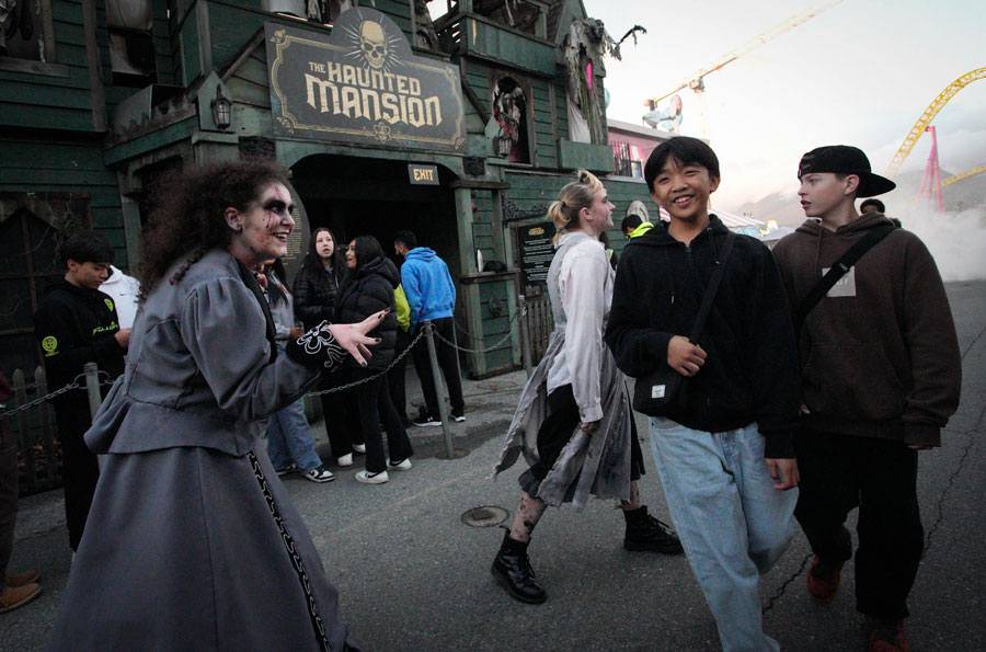 Visitors approach a haunted house attraction where costumed actors roam the entrance, adding to the frightful atmosphere. These interactive experiences, popular across Long Island each October, combine theatrical performances, spooky effects, and detailed sets to immerse guests in Halloween thrills.