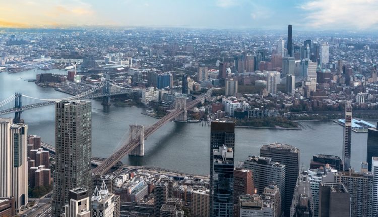 Panoramic aerial view of the Brooklyn Bridge stretching over East River, with the cityscape of Brooklyn in the backdrop.