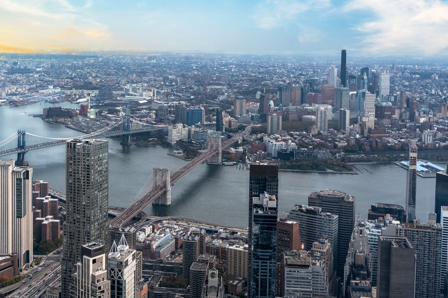Panoramic aerial view of the Brooklyn Bridge stretching over East River, with the cityscape of Brooklyn in the backdrop.
