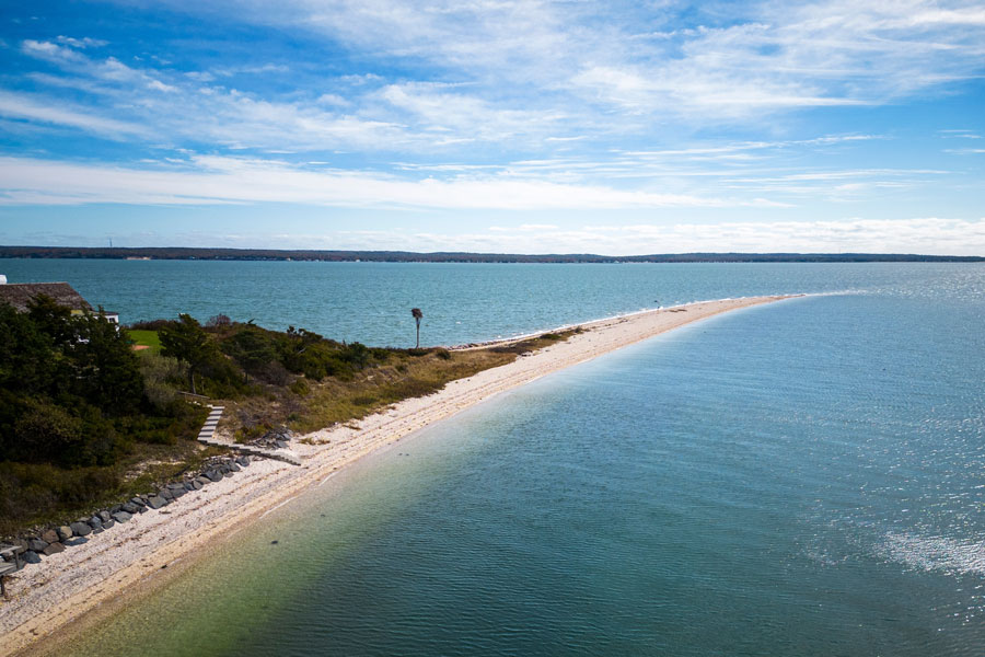 Drone view of Nassau Point on the North Fork of Long Island where Great Peconic Bay and Little Peconic Bay meet, showing a narrow sand spit and surrounding water.