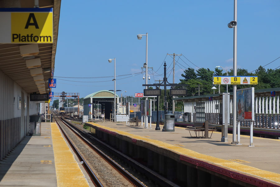 Wide-angle photo of the Ronkonkoma LIRR station platforms, showing empty tracks, signage, and waiting areas under clear skies.