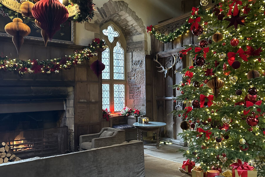 Interior of Planting Fields Arboretum in Oyster Bay, NY, beautifully decorated for Christmas with a large illuminated tree, garlands, and fireplace during the Holiday Market event.
