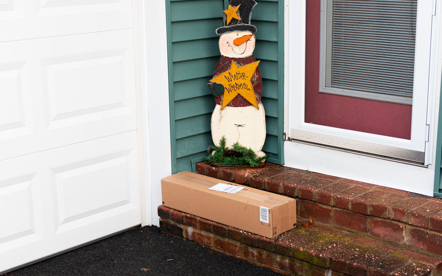 Unattended delivery package left on a doorstep next to a snowman decoration, representing the type of porch-delivered boxes targeted in the Suffolk County package-theft ring.