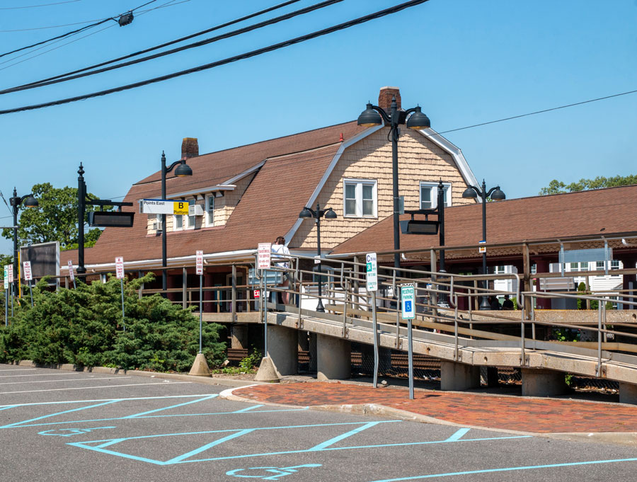 Bay Shore LIRR station with parking lot and accessible ramp on a sunny day, serving passengers traveling to the Fire Island Ferry.