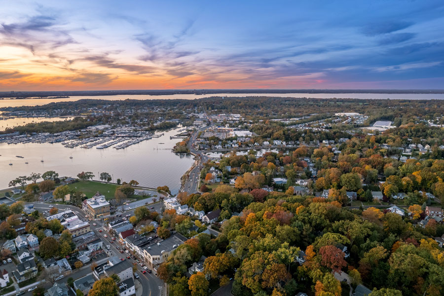 Aerial view of Manhasset Bay at sunset showing marinas, neighborhoods, and shoreline roads on Long Island’s North Shore.
