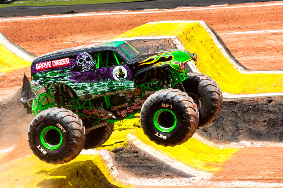 Grave Digger monster truck airborne during a Monster Jam racing competition on a dirt track.