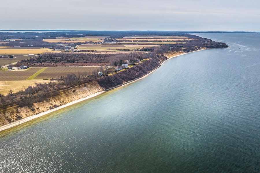 Aerial view of the North Shore of Long Island overlooking Gardiners Bay, where rolling farmland meets dramatic coastal bluffs and the calm waters stretch toward Gardiners Island in the distance. This sweeping perspective captures the quiet, untouched beauty of one of the East End’s most historic and secluded waterfront landscapes.