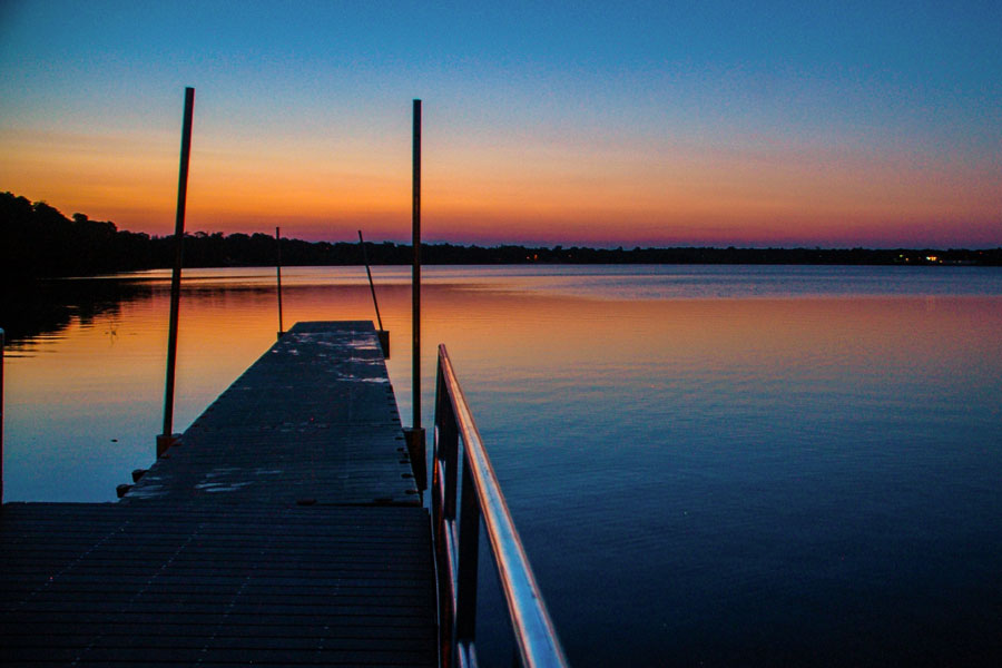 Sunset settles over Lake Ronkonkoma as a quiet dock stretches into calm waters, capturing the peaceful atmosphere that defines this iconic Long Island landmark. The fading light reflects across the lake’s surface, highlighting one of Suffolk County’s most scenic and storied natural settings.