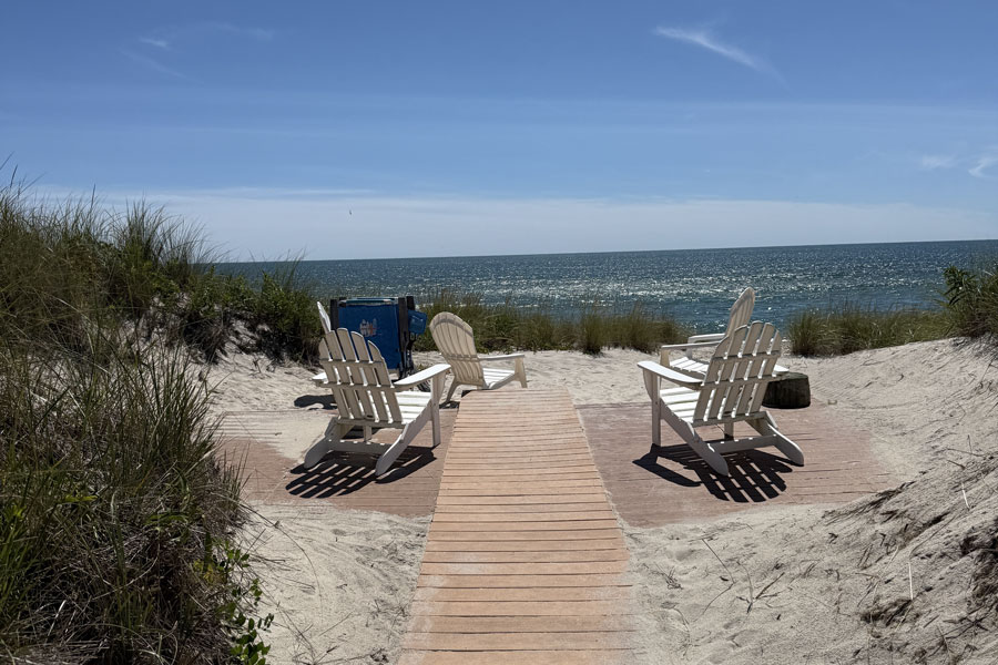 A sandy boardwalk leads through the dunes toward the Atlantic shoreline in Westhampton Beach, where ocean views, coastal grasses, and quiet beach seating reflect the relaxed South Fork atmosphere of this popular Hamptons destination.
