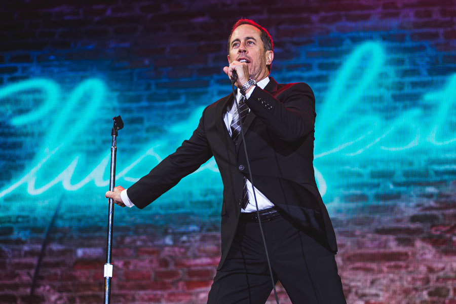 Jerry Seinfeld performs during a live stand-up appearance, representing the generation of comedians who helped fuel America’s stand-up comedy boom during the 1980s and 1990s. Long Island comedy clubs were once part of the larger New York-area circuit that helped rising comics develop material and build audiences before achieving national fame. 