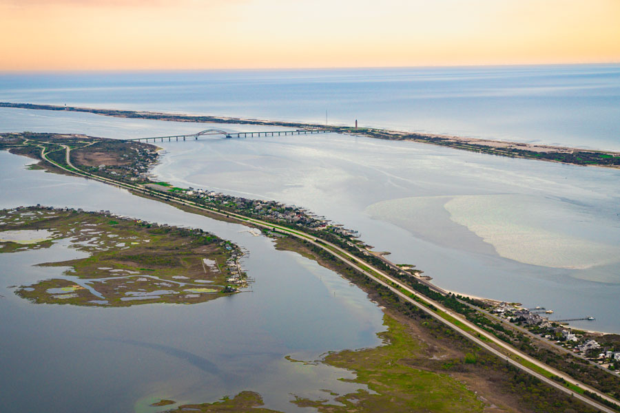 Aerial view of Bay Parkway and the Jones Beach barrier island on Long Island’s South Shore, with the Jones Beach water tower and bridge crossings visible in the distance as the roadway winds through the coastal marshlands of Nassau County, New York.
