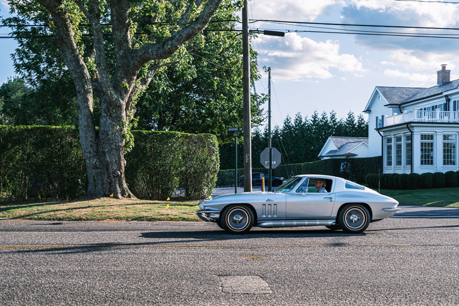 A classic Chevrolet Corvette driven along a residential street in Quogue, Long Island, New York, showcasing vintage American sports car design. 08-27-25