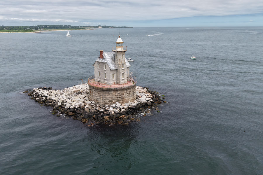 Race Rock Lighthouse stands at the western approach to Fishers Island, guiding vessels through the powerful currents of The Race. Visible in the background is the shoreline of Fishers Island, one of Long Island's most remote and distinctive communities, located at the eastern entrance to Long Island Sound.