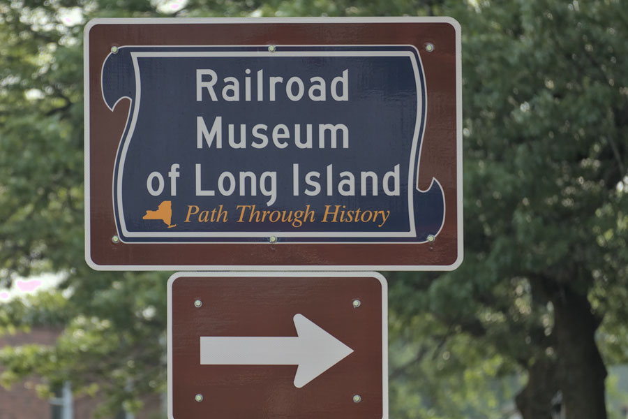 A roadside sign points the way to the Railroad Museum of Long Island in Riverhead, welcoming visitors to discover the region’s rich railroading history and explore exhibits that bring Long Island’s transportation heritage to life.