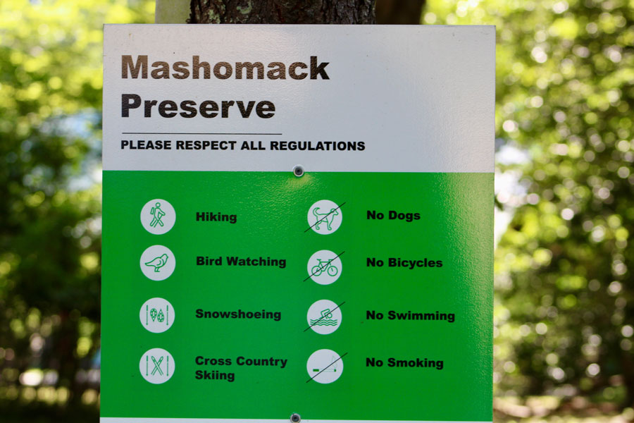 Mashomack Preserve trailhead sign surrounded by mature woodland on Shelter Island, New York. Managed by The Nature Conservancy, Mashomack Preserve protects more than 2,350 acres of forests, wetlands, tidal creeks, and shoreline habitat, making it one of the most important nature preserves on Long Island's East End. File photo: licensed.