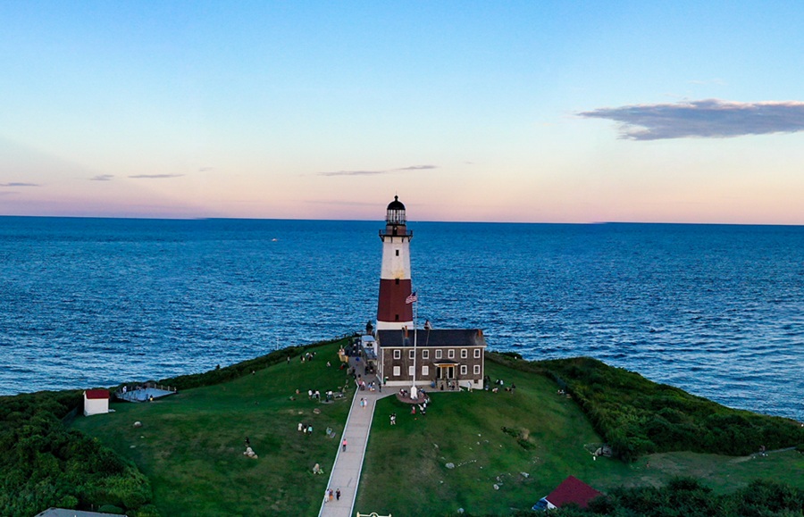 The iconic Montauk Point Lighthouse stands at the eastern tip of Long Island, overlooking the Atlantic Ocean as evening settles over the coast. Commissioned by President George Washington in 1792 and first illuminated in 1796, it remains New York State's oldest lighthouse and one of Long Island's most recognizable historic landmarks.