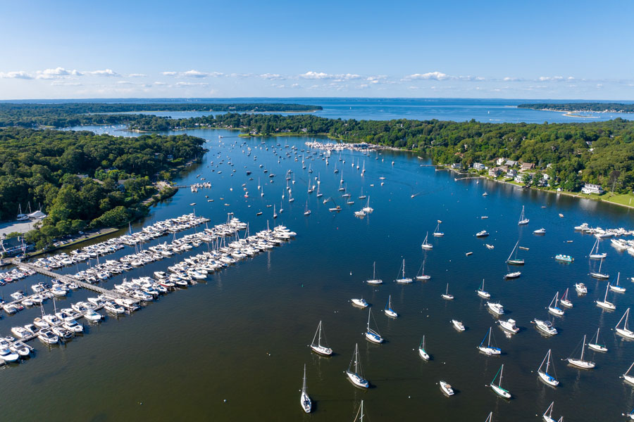 An aerial view overlooks Centerport Harbor, where marinas, sailboats, and moored vessels fill the protected waters before they open into Huntington Bay and Long Island Sound. Surrounded by the waterfront communities of Centerport and Lloyd Harbor, the harbor is one of the Town of Huntington's premier destinations for boating, sailing, fishing, and enjoying the scenic beauty of Long Island's North Shore. File photo: Michael Chow Media, licensed.