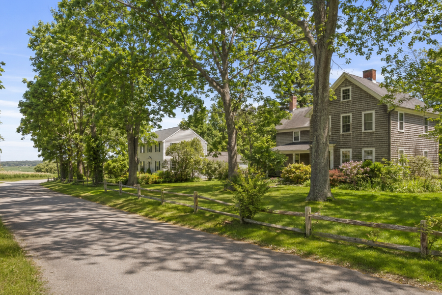 Traditional homes line a quiet, tree-shaded road in Northville, New York. Spacious lawns, mature landscaping, split-rail fencing, and nearby farmland reflect the community’s rural residential character. The peaceful setting illustrates the blend of country living and coastal North Fork scenery found throughout the hamlet.