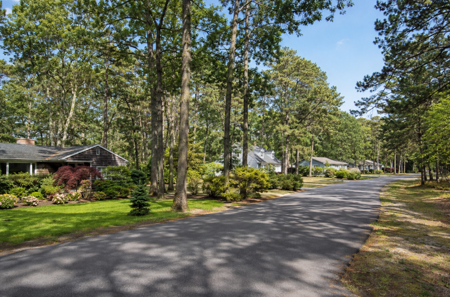 Detached homes line a quiet, tree-shaded residential road in Northampton, New York. Mature oaks and pines, spacious lawns, and established landscaping contribute to the neighborhood’s peaceful appearance. The wooded setting reflects the rural character found throughout this lightly developed Suffolk County community.