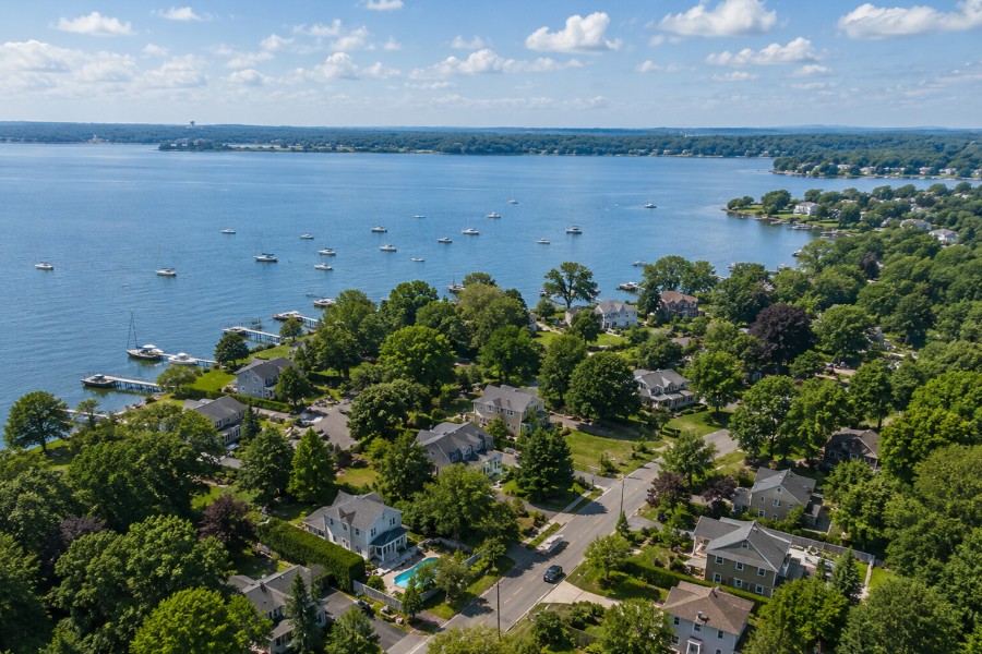 An aerial view of Poquott, New York, showcases the village's quiet waterfront neighborhoods along Setauket Harbor, where tree-lined streets, well-maintained homes, private docks, and scenic shoreline combine to create one of Long Island's most picturesque North Shore residential communities.
