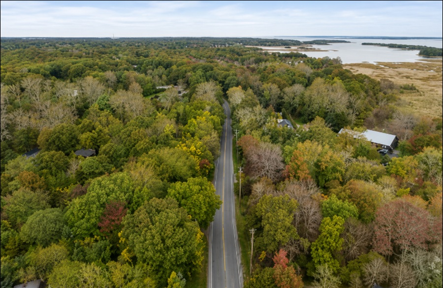 An aerial view of Springs, New York, showcases a winding roadway passing through dense woodlands before reaching the tidal marshes and tranquil waters of Gardiners Bay. Expansive forests, protected wetlands, and scattered homes illustrate the hamlet's unspoiled coastal landscape, highlighting the natural beauty and peaceful waterfront setting that make Springs one of the East End's most scenic communities on Long Island.