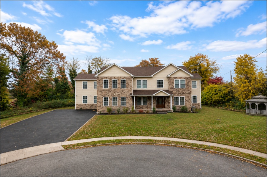 A spacious home in Wheatley Heights, New York, sits on a quiet cul-de-sac surrounded by mature trees and expansive, well-maintained grounds. The large two-story residence, broad front lawn, and peaceful suburban setting reflect the community's reputation for generous residential properties and its tranquil neighborhood atmosphere in western Suffolk County on Long Island.