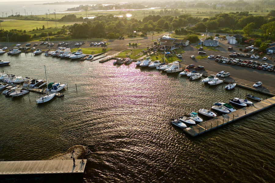 An aerial view of boats docked at East Islip Marina and Park in Suffolk County, Long Island, during a summer sunset. Warm evening light reflects across the water as rows of recreational boats line the marina’s slips, with the park, parking areas, and surrounding shoreline visible in the background. File photo: Audley C Bullock, licensed.