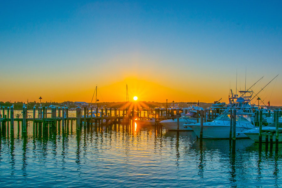 Boats rest quietly in the marinas of Montauk Harbor as the sun sets over one of Long Island's busiest boating and commercial fishing ports. Protected from the open Atlantic by Montauk Inlet, the harbor serves as a major destination for charter fishing, recreational boating, waterfront dining, and marine tourism throughout the year.