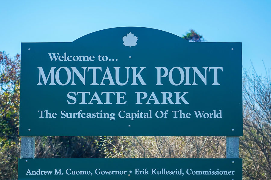 A welcome sign marks the entrance to Montauk Point State Park at the eastern tip of Long Island. Known as the "Surfcasting Capital of the World," the park is a renowned destination for saltwater fishing, scenic coastal views, hiking, wildlife observation, and access to the historic Montauk Point Lighthouse.
