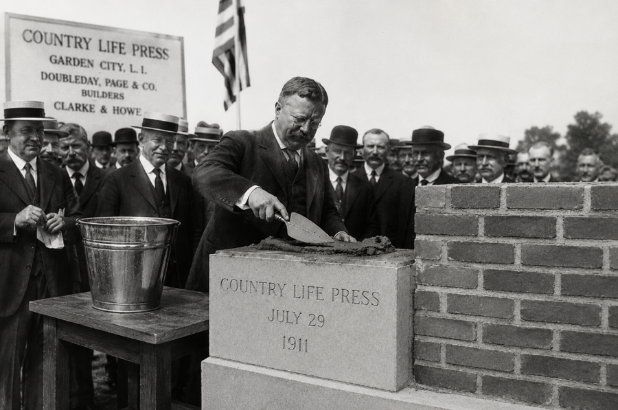 A recreated black-and-white illustration based on a historic photograph published in The Country Life Press: Garden City, New York (1913), depicting former President Theodore Roosevelt laying the cornerstone for the Country Life Press publishing complex in Garden City on July 29, 1911. The ceremony marked the beginning of what would become one of the nation's largest and most influential publishing and printing facilities.